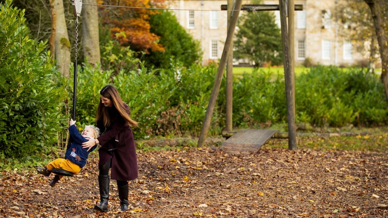 Child on the zipline with adult alongside with Wallington's house in the background